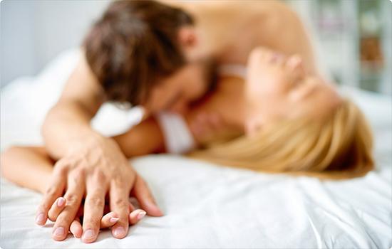 Close-up of a couple in a sensual moment, with hands intertwined on a white bed.